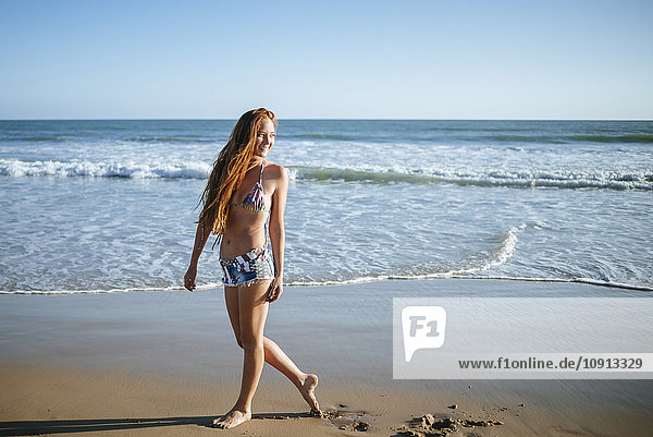 Lächelnde junge Frau beim Spaziergang am Strand