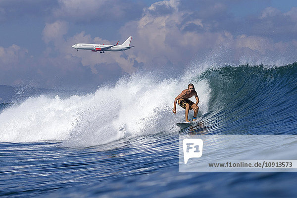 Indonesien Bali Surfer auf Welle Flugzeug im Hintergrund