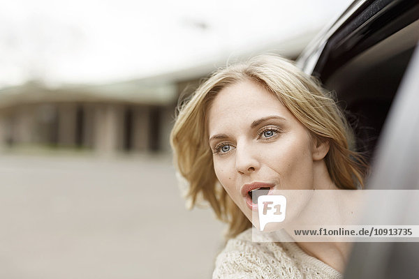Porträt einer schreienden jungen Frau  die sich aus dem Autofenster lehnt.
