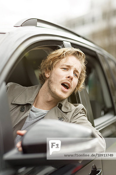 Porträt eines schreienden jungen Mannes  der sich aus dem Autofenster lehnt.
