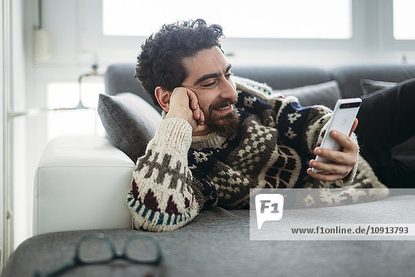 Smiling man lying on a couch looking at phablet