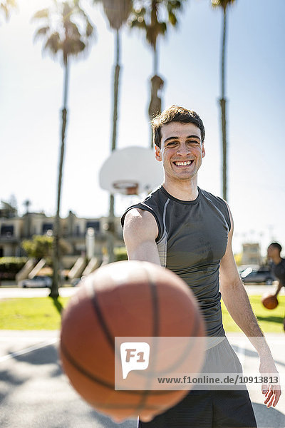 Lächelnder junger Mann hält Basketball auf dem Freigelände
