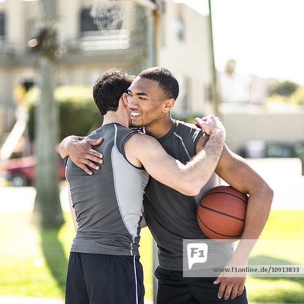 Zwei Basketballspieler  die sich im Freien umarmen.
