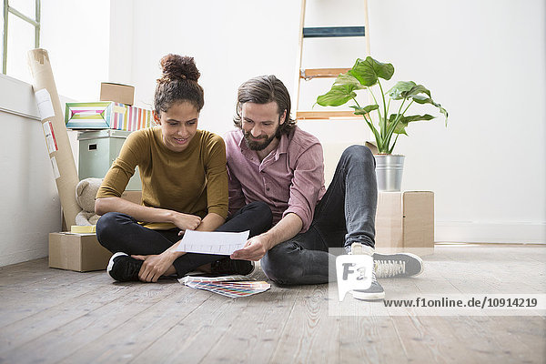 Couple sitting on floor of new flat choosing from color samples