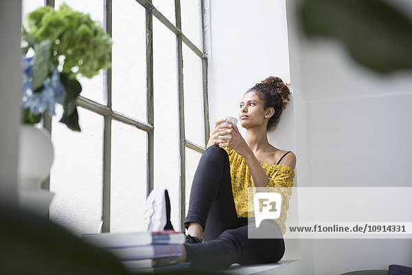 Young woman sitting on window sill with a cup of coffee