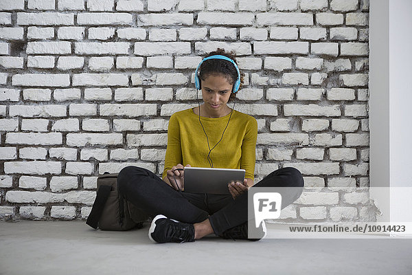 Junge Frau mit Kopfhörer auf dem Boden sitzend mit digitalem Tablett