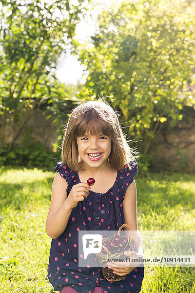 Porträt eines lachenden kleinen Mädchens  das im Garten Kirschen isst.