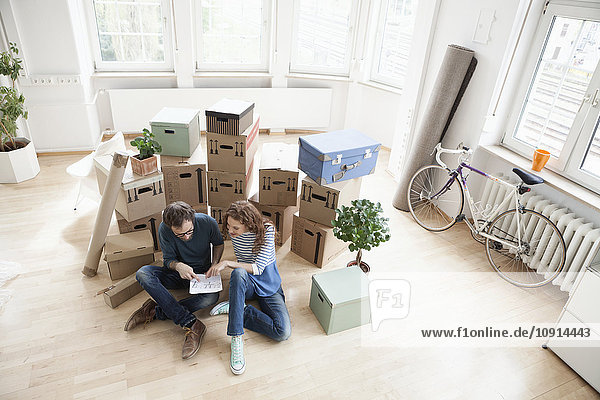 Couple surrounded by cardboard boxes with plan on floor