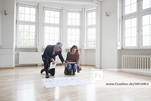Real estate agent showing construction plan to client in empty apartment