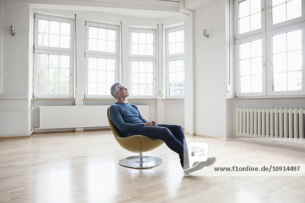 Mann sitzend im Sessel in leerer Wohnung