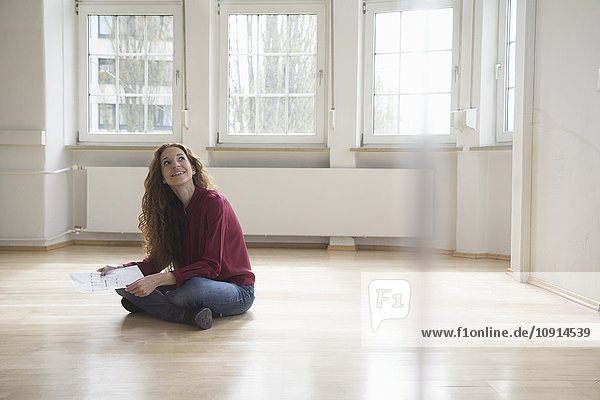 Woman sitting on floor in empty apartment looking around