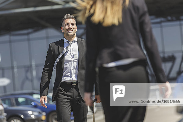 Lächelnder Geschäftsmann mit Gepäck auf dem Parkplatz mit Blick auf die Frau