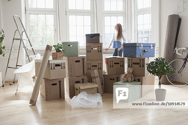 Woman with cardboard boxes in new apartment looking out of window