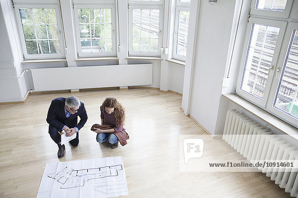 Real estate agent showing construction plan to client in empty apartment