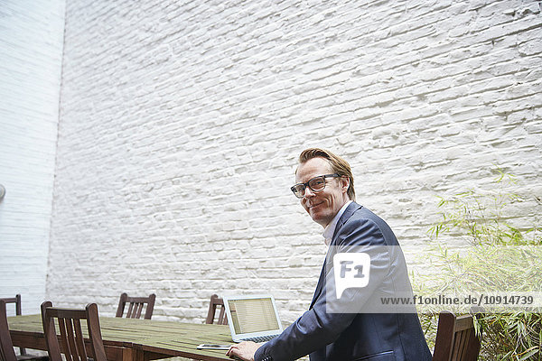 Businessman sitting with laptop at table in a backyard