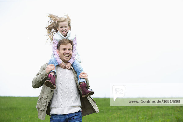 Glücklicher Vater trägt Tochter auf den Schultern auf der Wiese