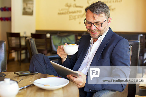 Porträt eines lächelnden Geschäftsmannes,  der in einem Café sitzt und Kaffee trinkt.