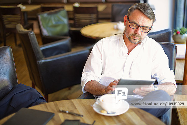 Geschäftsmann sitzt in einem Coffeeshop und benutzt ein digitales Tablett.