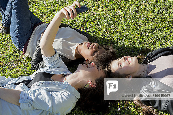 Three girl friends lying on grass taking selfie with smart phone