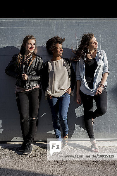 Drei junge Frauen  die sich an die Wand lehnen.