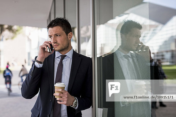 Businessman outdoors with cell phone and coffee to go