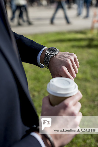 Businessman outdoors with coffee to go checking the time