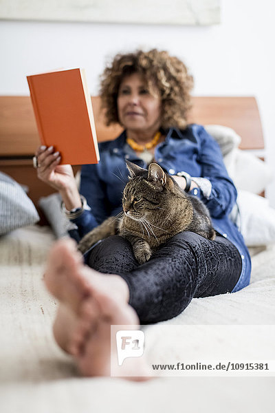 Woman with cat on bed reading book