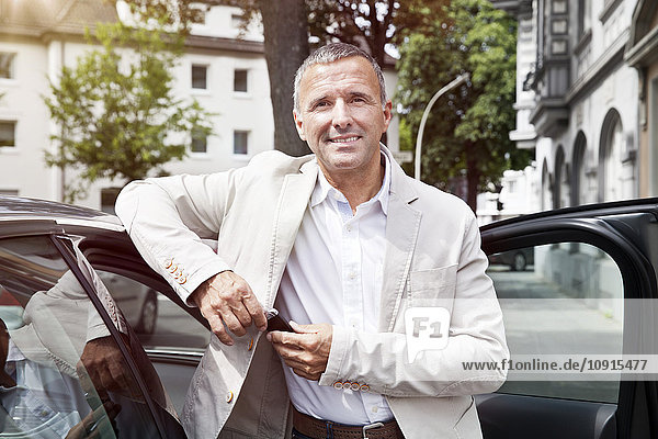 Portrait of smiling man leaning at open car door with car keys