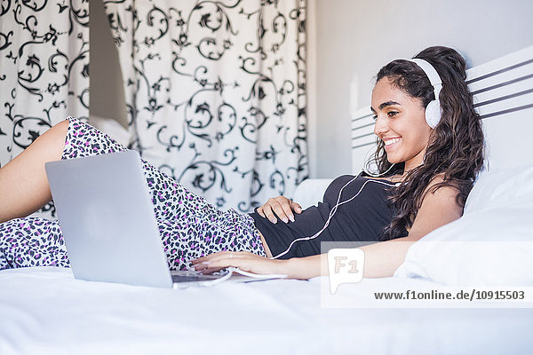Teenager Mädchen mit Kopfhörer auf dem Bett liegend mit Laptop