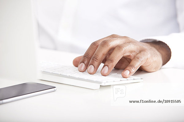 Man's hand typing on keyboard at white desk