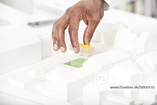Man's hand putting building block on architectural model  close-up