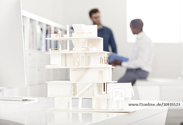 Architectural model on desk in an office with two talking people in the background