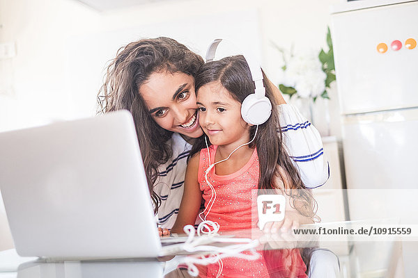 Fröhliches Teenagermädchen und ihre kleine Schwester mit Laptop und Kopfhörer