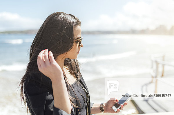 Junge schöne Frau sendet eine Nachricht mit dem Smartphone am Strand