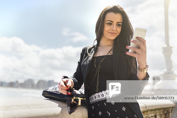Junge schöne Frau sendet eine Nachricht mit dem Smartphone im Hafen