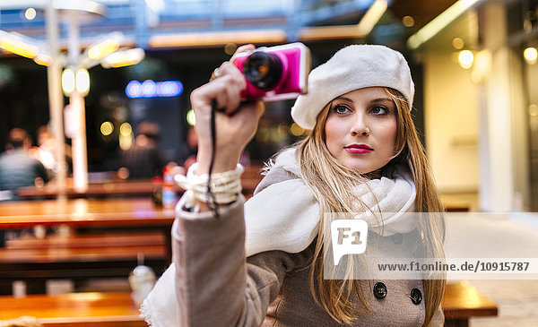 Porträt einer jungen Frau mit Baskenmütze  die sich selbst mit einer Digitalkamera fotografiert.