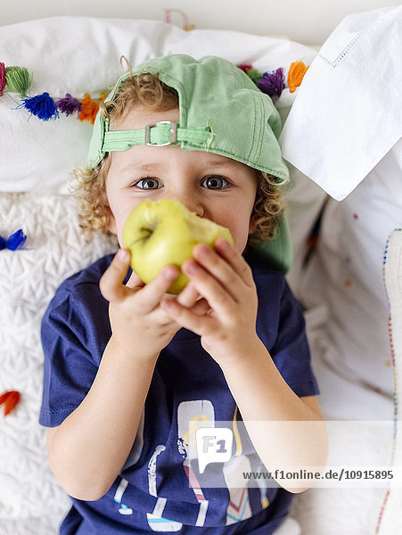 Porträt eines kleinen Jungen  der auf der Couch sitzt und einen Apfel isst.