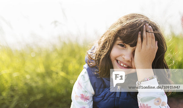 Portrait of smiling little girl covering eye with her hand