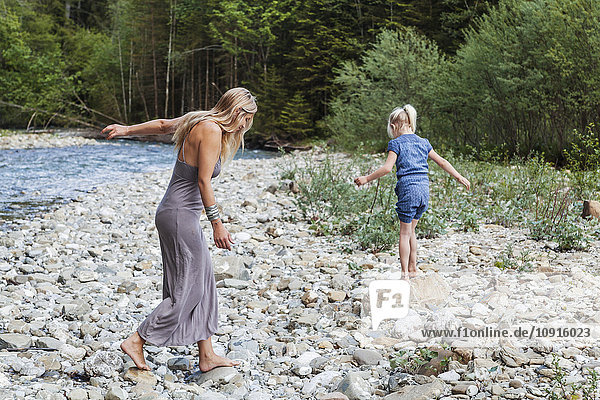 Mutter und ihre kleine Tochter beim Spaziergang am steinigen Flussufer
