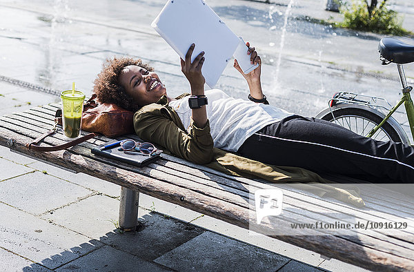 Lächelnde Frau liegt auf einer Bank und liest Notizen.
