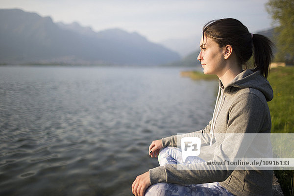 Italy  Lecco  relaxed young woman sitting at the lakeshore