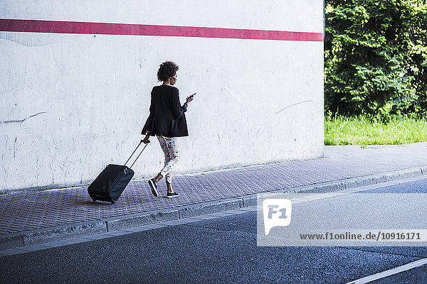 Geschäftsfrau mit Gepäck und Smartphone  die die Straße entlang läuft