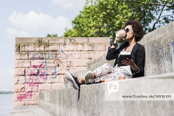 Junge Geschäftsfrau mit digitaler Tablette beim Kaffee trinken am Flussufer