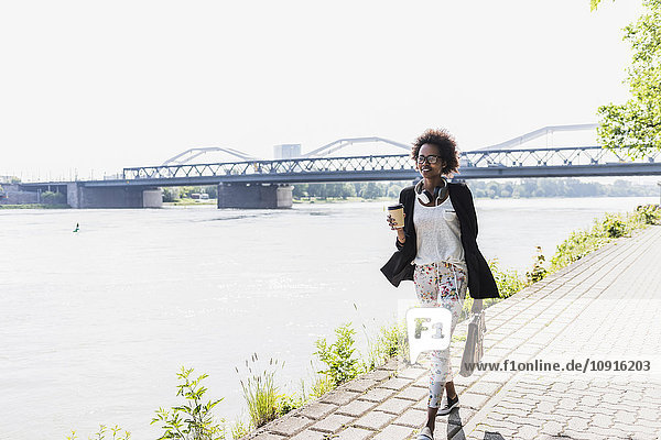 Deutschland  Mannheim  junge Geschäftsfrau mit Aktentasche und Kaffee zum Spazierengehen am Flussufer