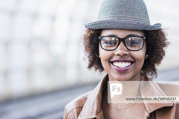 Porträt einer lächelnden jungen Frau mit Hut und Brille