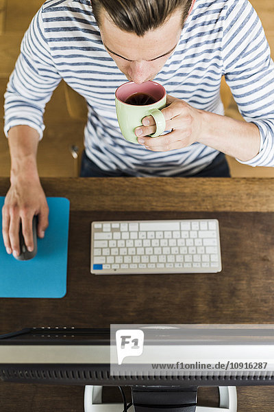 Mann mit Computer und Kaffeetrinken aus der Tasse am Schreibtisch
