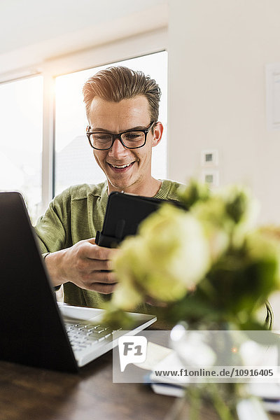 Lächelnder Mann am Schreibtisch mit Laptop und digitalem Tablett