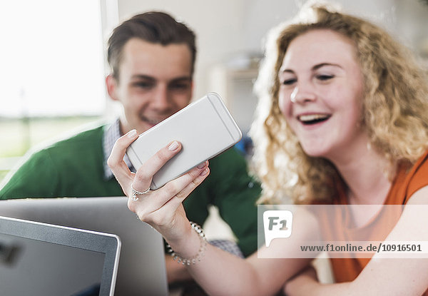 Zwei lächelnde junge Profis beim Blick aufs Handy