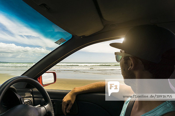 Neuseeland  Mann sitzt in seinem Auto und schaut aufs Meer.