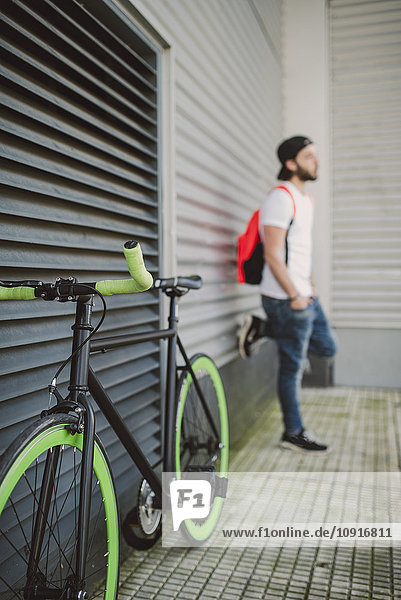 Fixie bike and young man leaning against wall